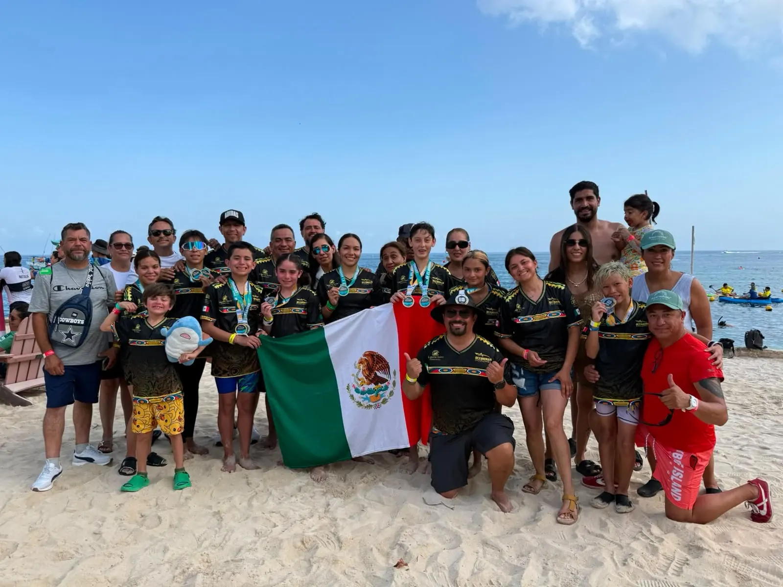 El equipo Laguna Swim con medallas y la bandera de México en la playa de Cozumel, en Oceanman